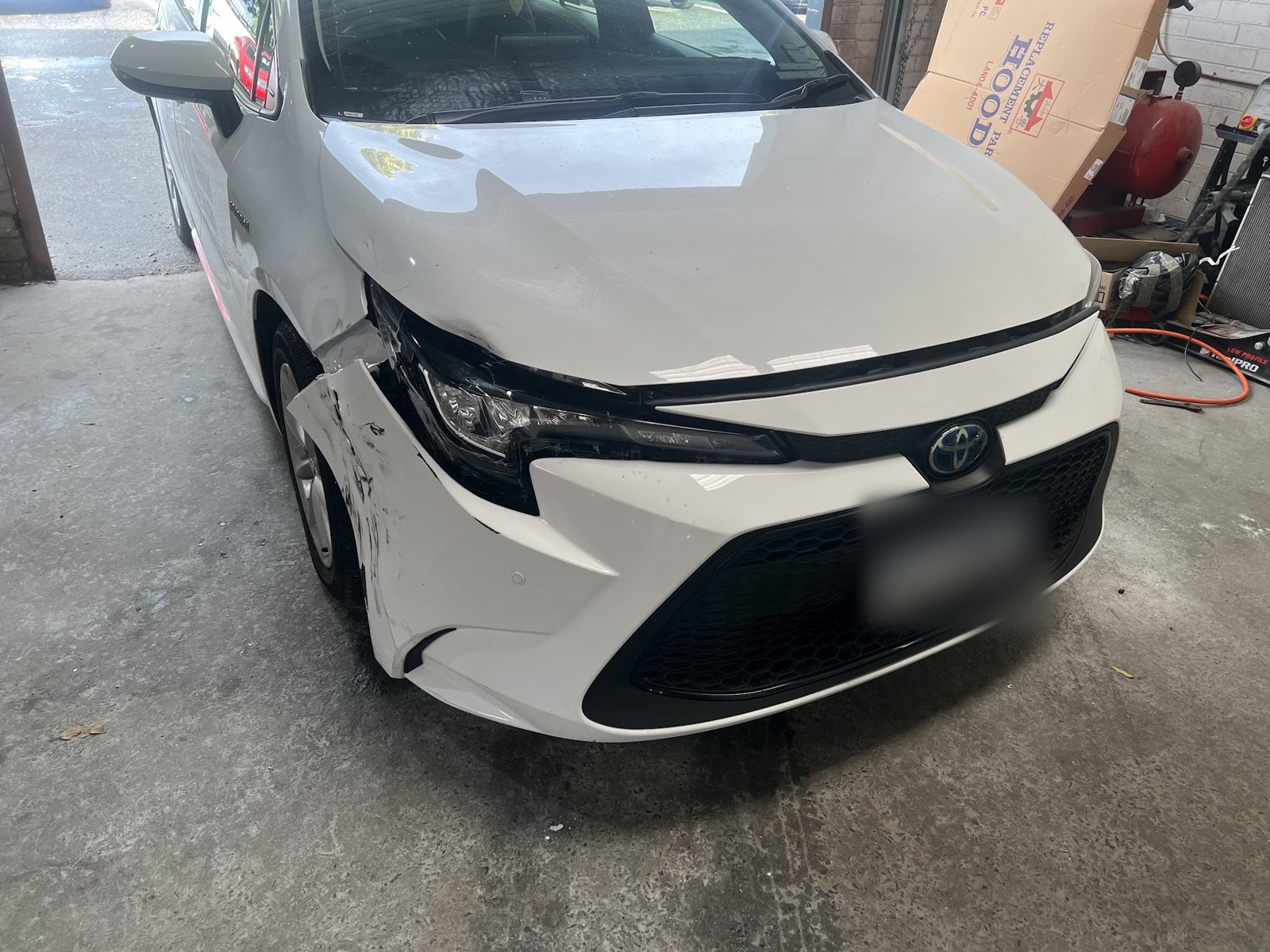 White Toyota Corolla with a cracked headlight and torn bumper corner in the workshop