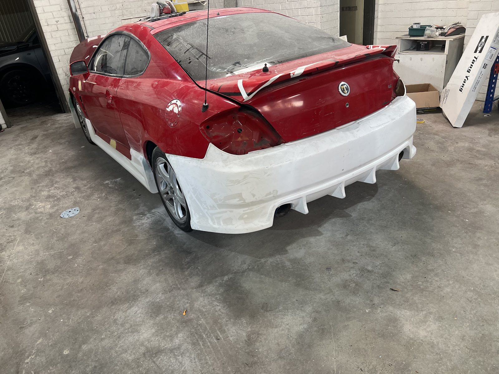 Red Hyundai coupe with its rear bumper in white primer, ready for colour