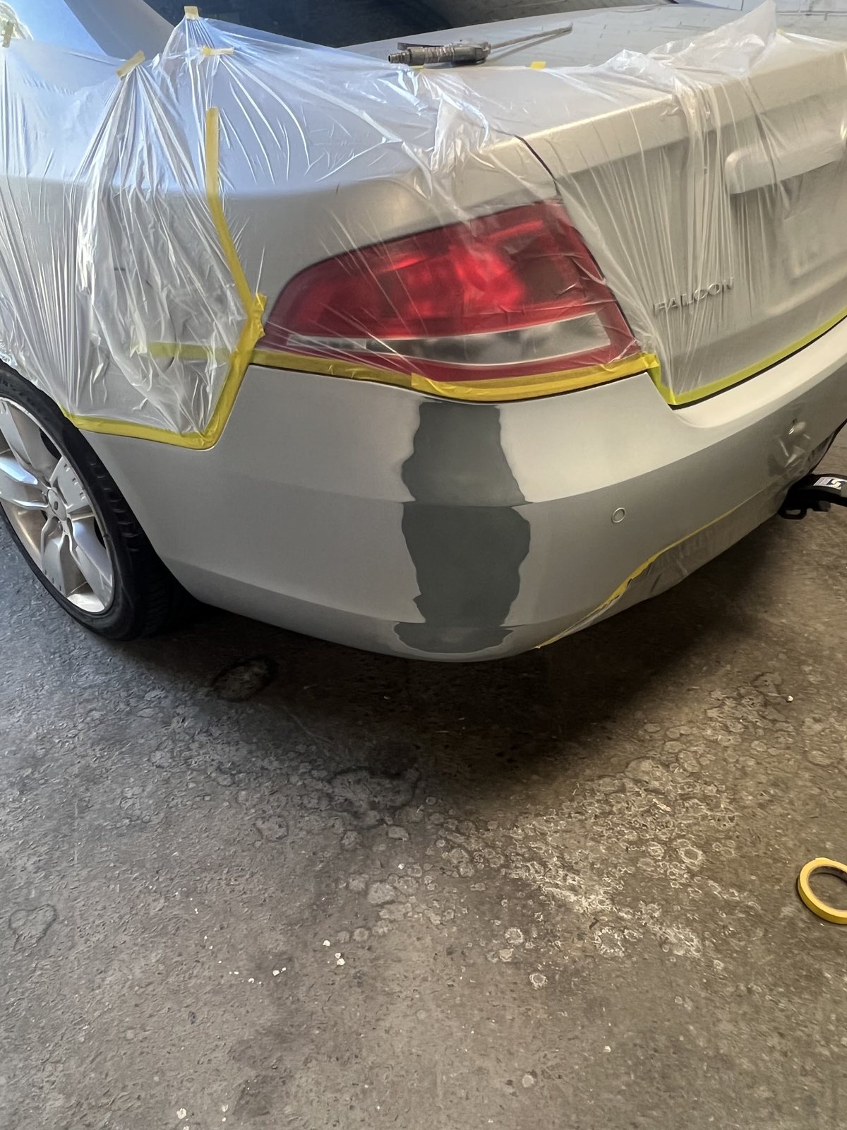 Silver Ford Falcon with its rear bumper masked in plastic and yellow tape, primer patch on the corner