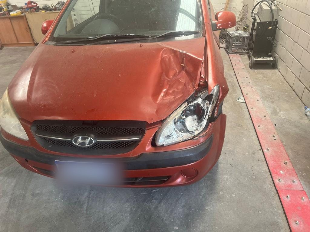 Red Hyundai Getz with a crumpled bonnet and front corner on the workshop floor