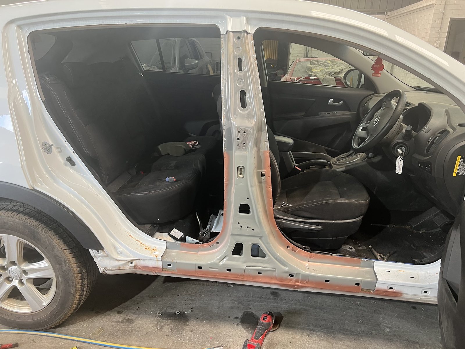 White Kia with its door off, the pillar and sill taken back to bare metal and primer
